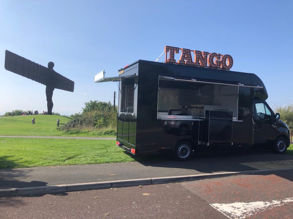 Black catering trailer beside modern trailers with the Angel of the North behind